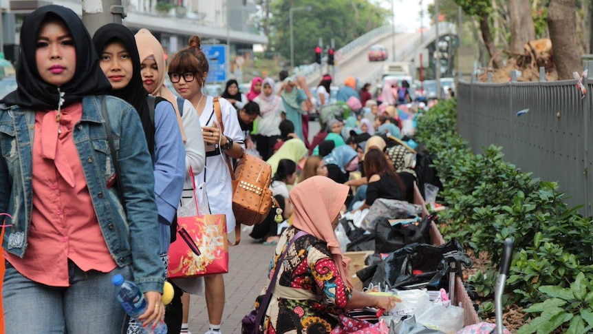 Women migrant workers walk towards the camera as others sit on the footpath in Hong Kong.