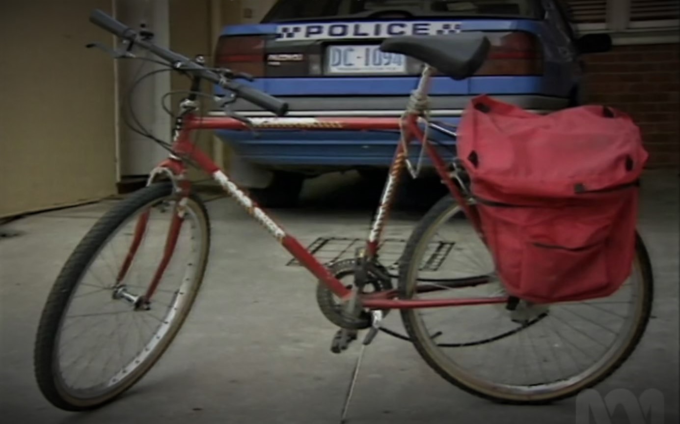 A red bicycle stands behind a police car.