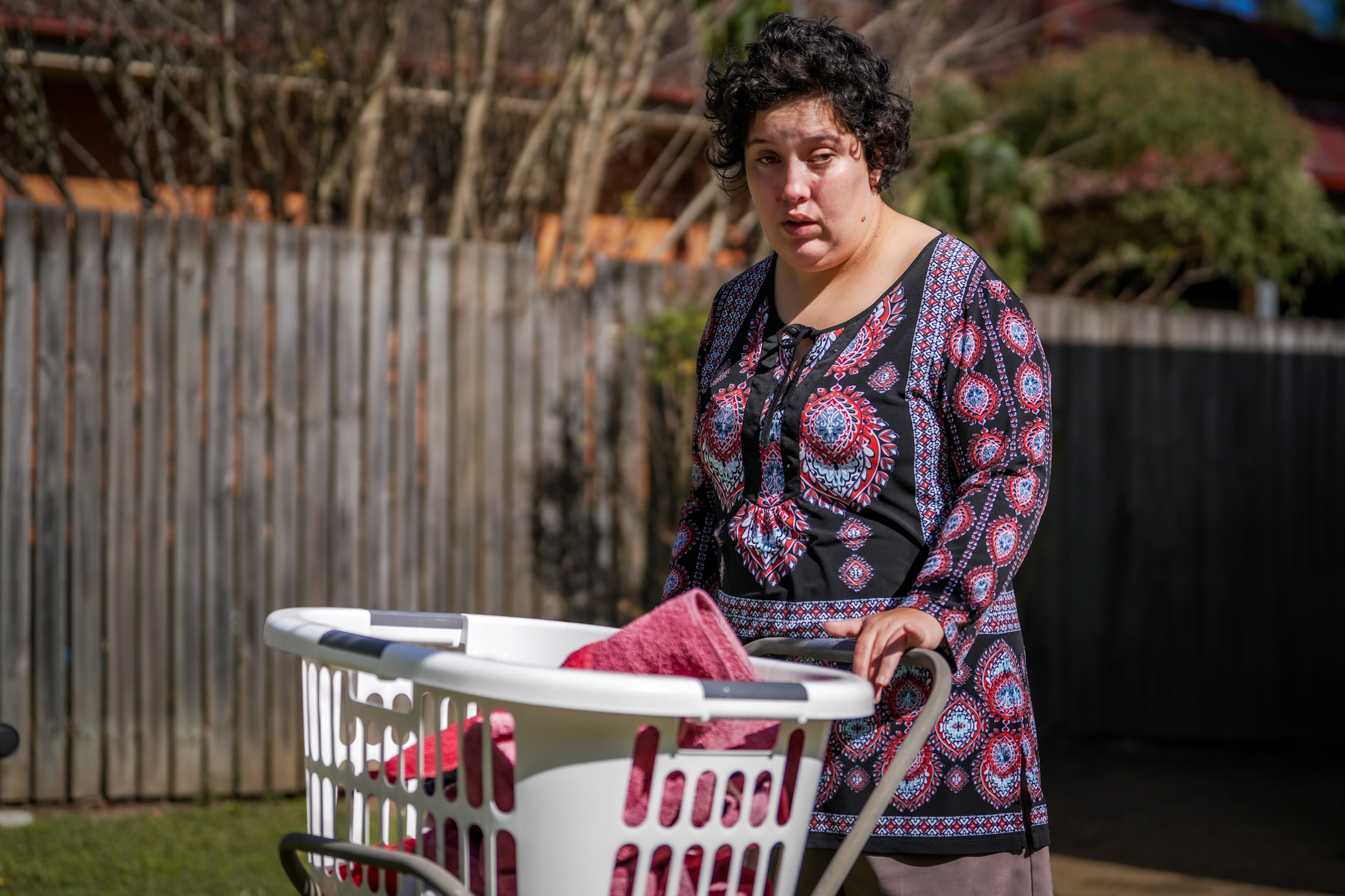 A woman with short brown hair wearing a black and red patterned dress with a laundry basket.