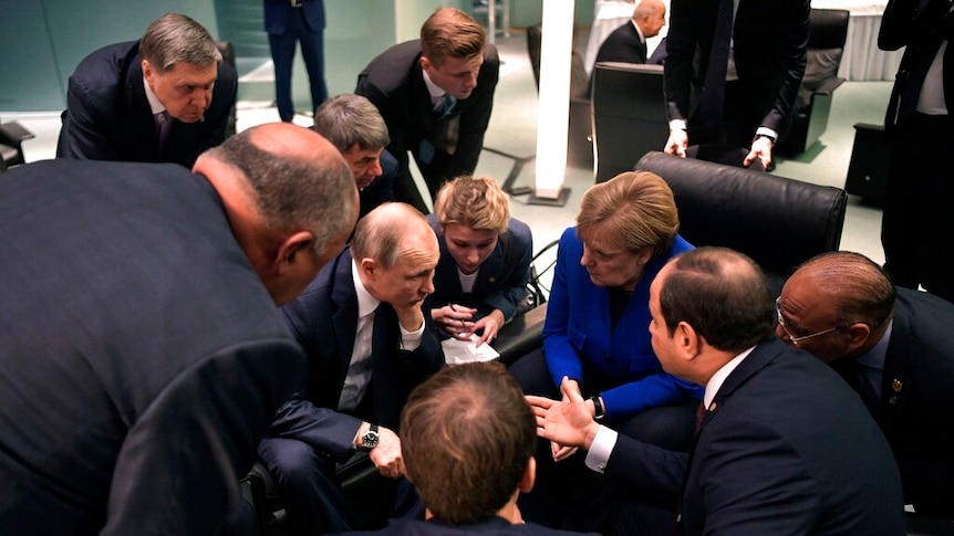 From above, you look down at Vladimir Putin and Angela Merkel as they are surrounded by staff in dark suits.