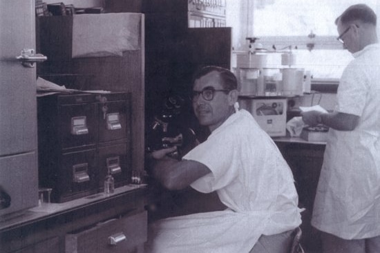 two men in lab coats in a black and white photo of a pathology lab