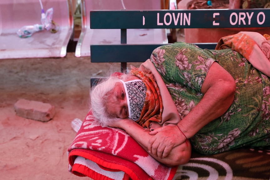 An elderly woman wearing a face mask lies on a bench