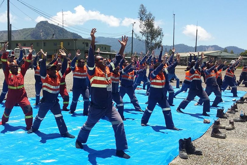 A group of mine workers in construction uniforms doing yoga