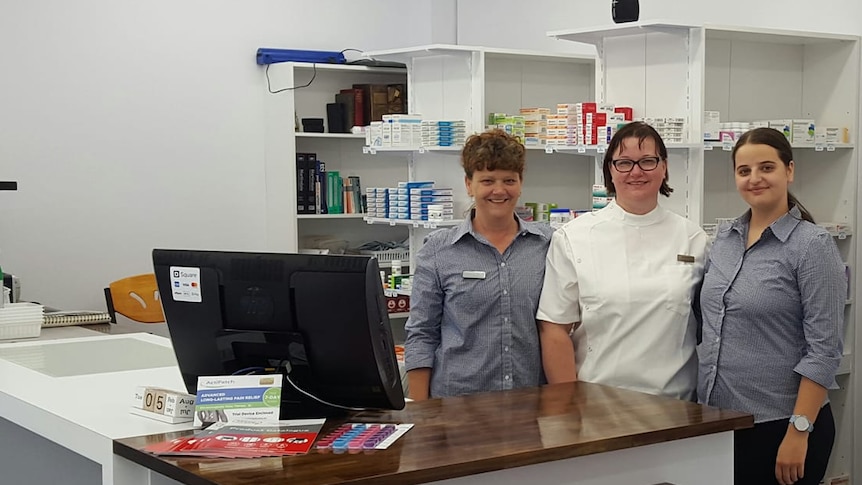Pharmacy owner Lyn Pilcher standing behind the counter with two of her female employees,  all smiling at the camera.