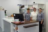 Pharmacy owner Lyn Pilcher standing behind the counter with two of her female employees,  all smiling at the camera.