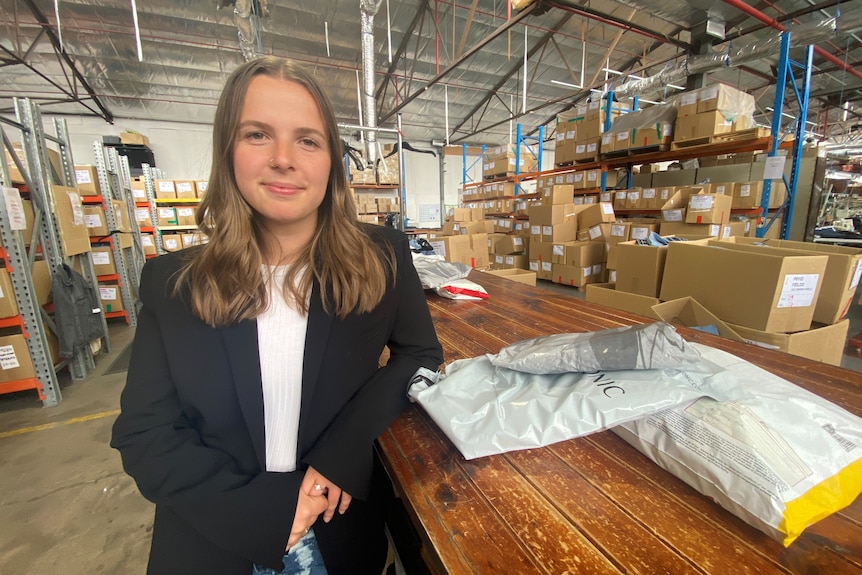 a young woman in a suit top next to a pile of packaging