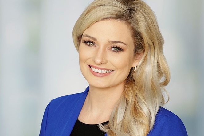 A corporate head shot of Dominique Lamb with styled long blonde hair and a blue jacket