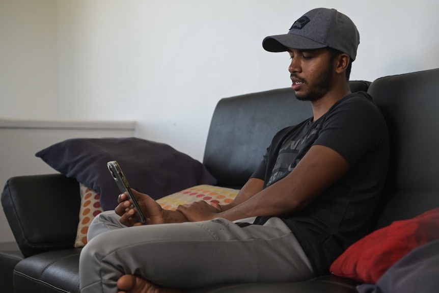 Samsul Alam sits on his lounge with his mobile phone in his home in Brisbane.