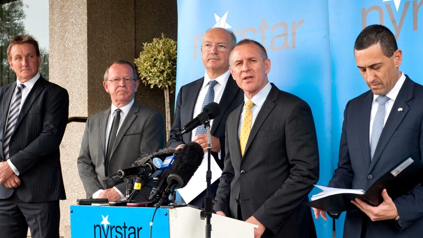 A group of men in suits stand on a small stage.  One is at a lecturn.