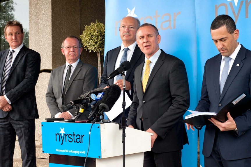 A group of men in suits stand on a small stage.  One is at a lecturn.