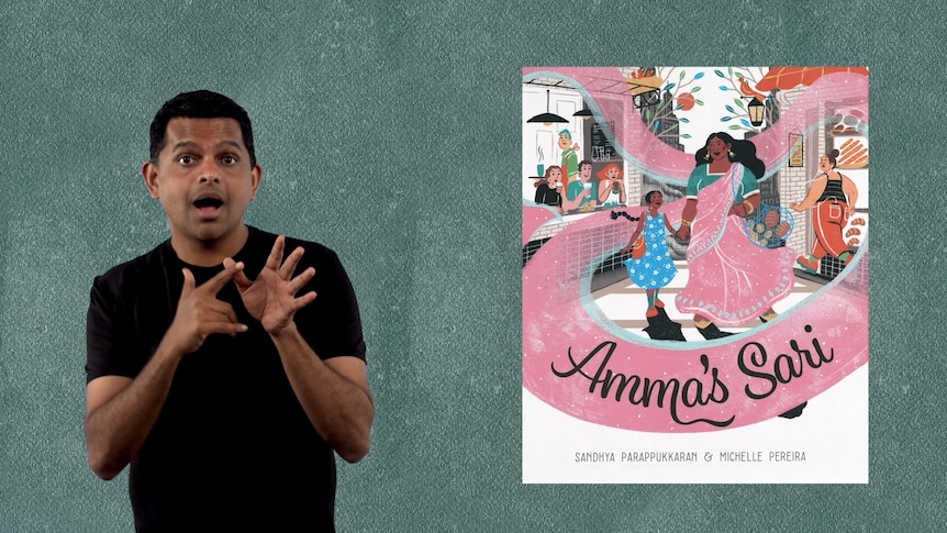 Auslan presenter Karthik Vijayanandam stands beside picture book called 'Amma's Sari'