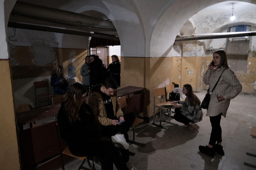 People in winter's clothes stand and sit in the basement of an old building at dawn 