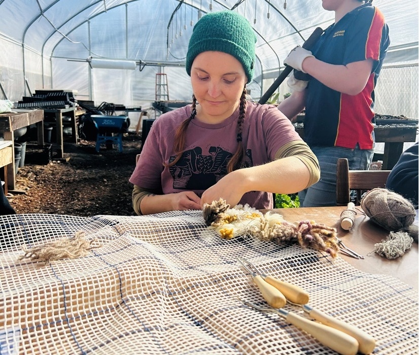A woman in a grow tunnel making a piece of art with wool.