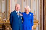 King Charles and Queen Camilla standing for a photo. Charles is wearing a blue suit, Camilla is wearing a long blue dress
