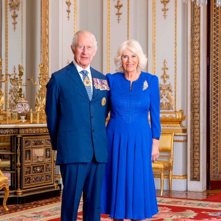 King Charles and Queen Camilla pose formally in dress wear in an ornate room with gold furnishing.