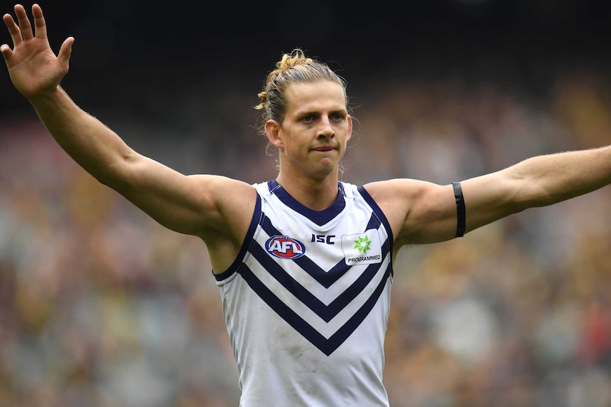 A mid shot of Fremantle Dockers captain Nat Fyfe standing with his arms outstretched in a white jersey.
