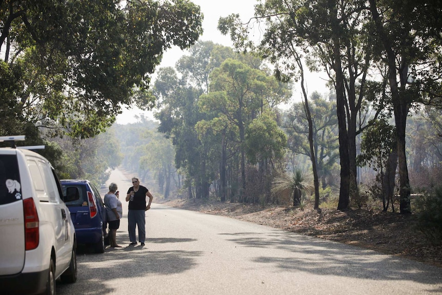 Two women stand beside their cars in Wundowie. Smoke can be seen down the road.