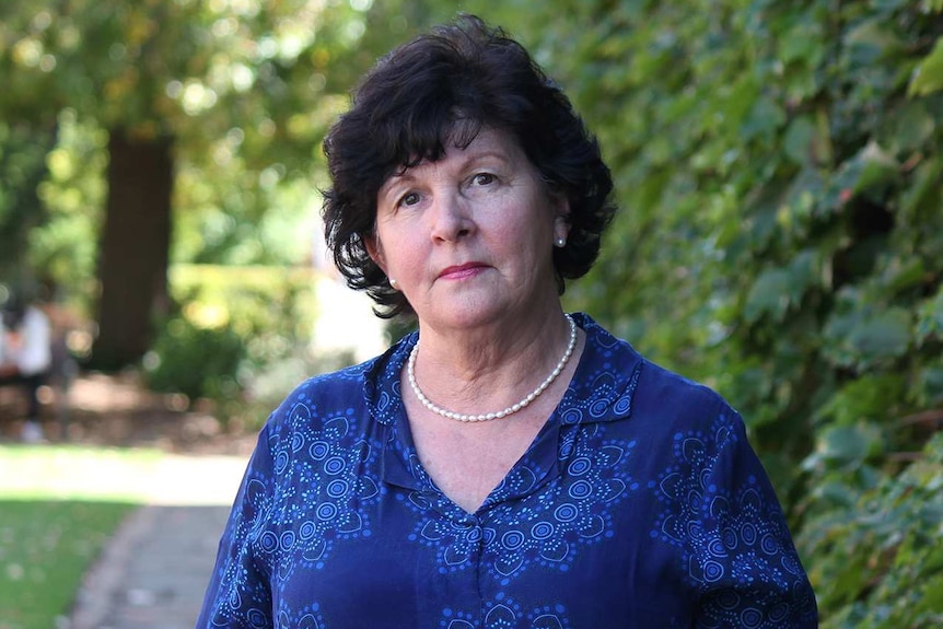 Toowoomba councillor Nancy Sommerfield looks concerned as she stands in a public garden in town wearing pearls and a blue shirt.