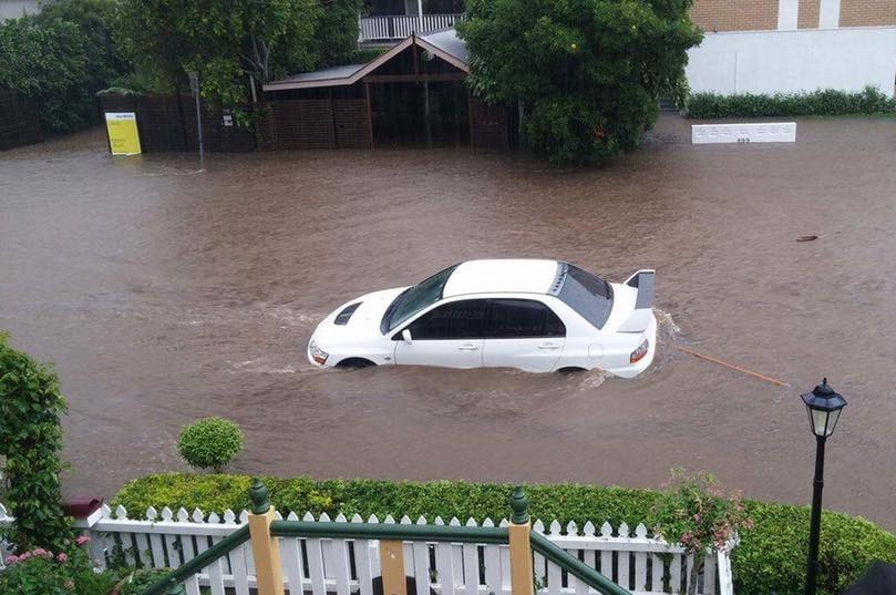 A white car is half-submerged in water on a flooded street in Paddington, Brisbane.