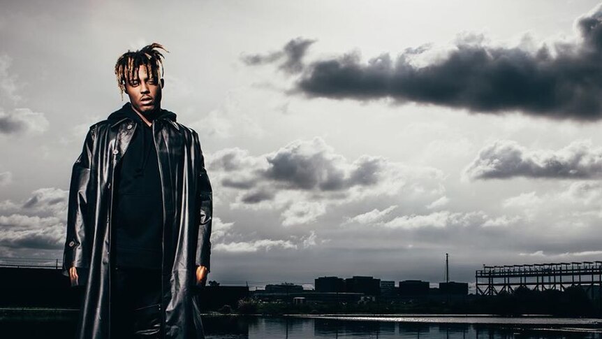 A moody photo of Juice Wrld in a large black leather trenchcoat standing in a shallow pool.