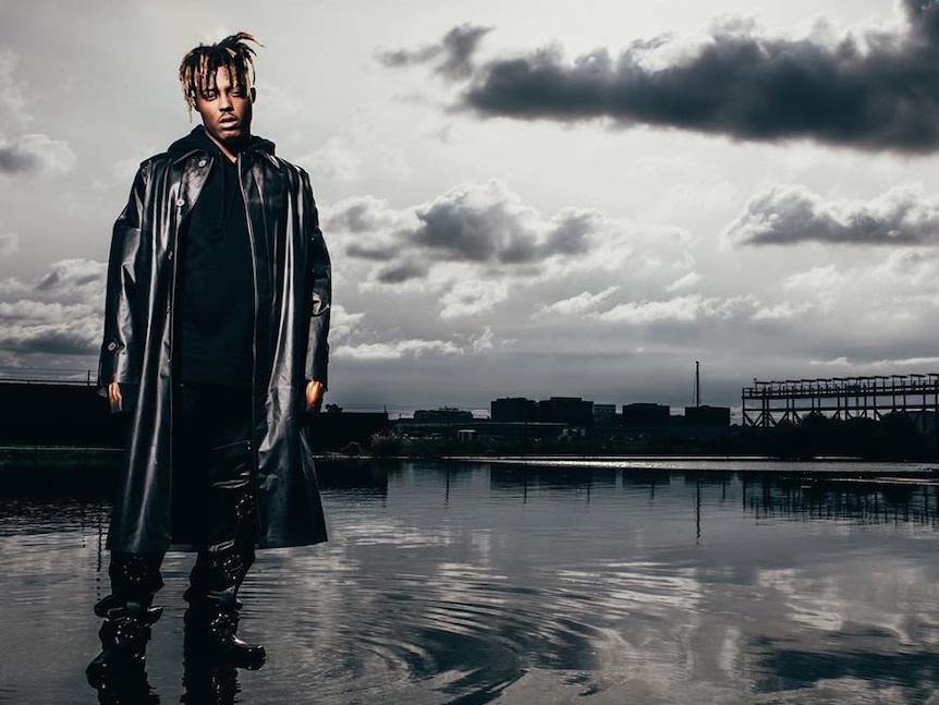 A moody photo of Juice Wrld in a large black leather trenchcoat standing in a shallow pool.