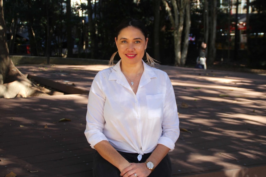 A young woman in a white shirt smiles while standing in a courtyard.