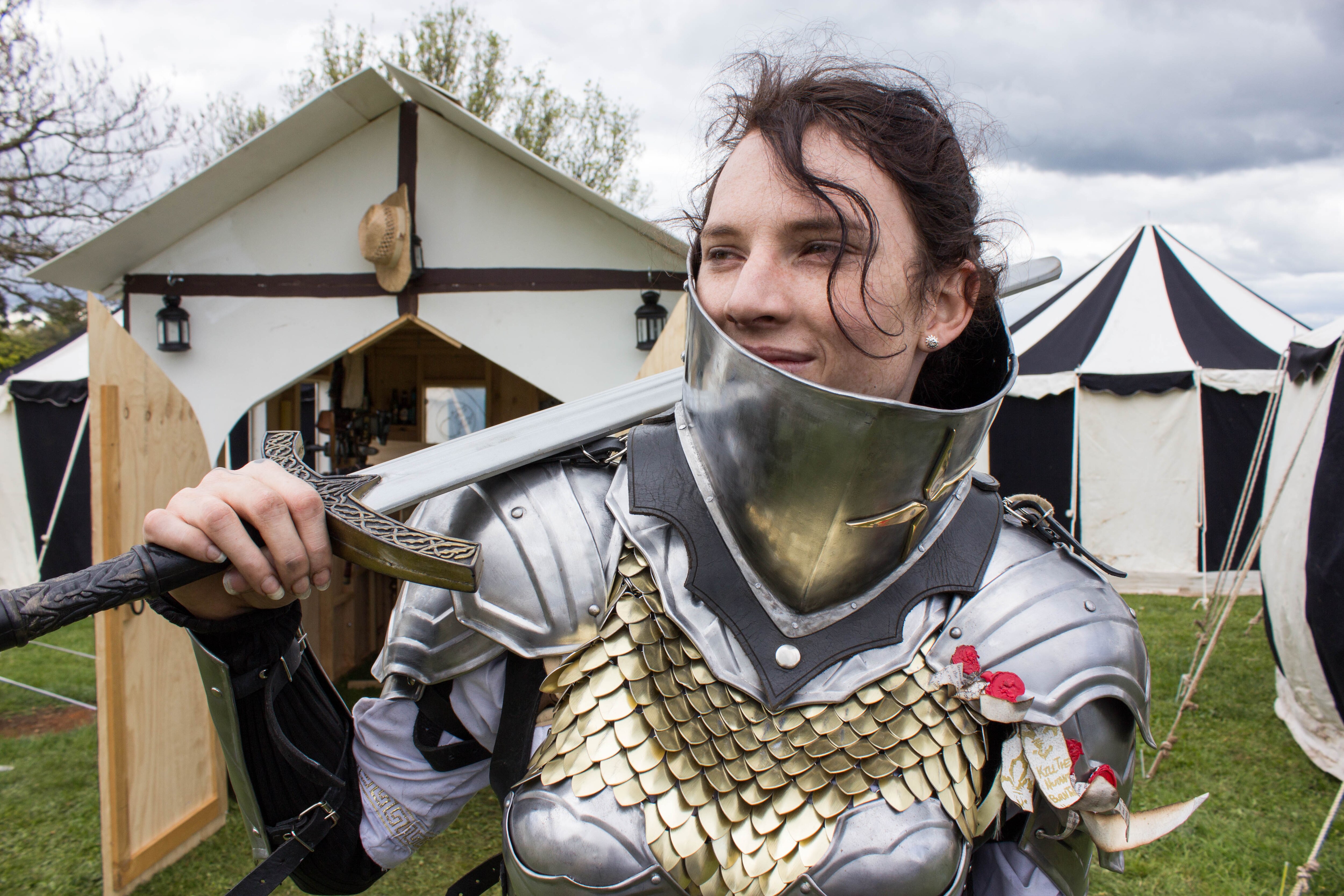 A woman rests a sword on her shoulder while looking into the distance