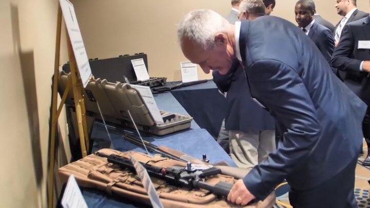 Steve Dickson, wearing a blue suit, leans down to inspect a gun.