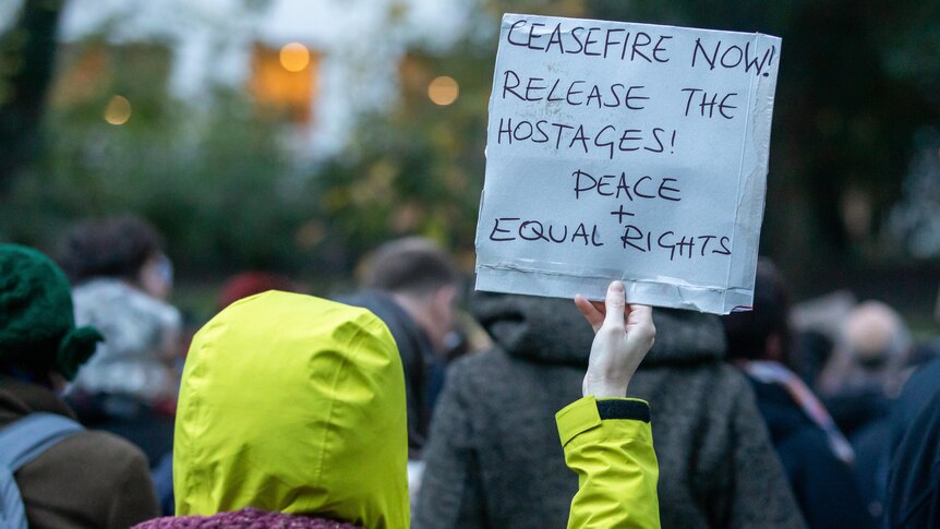 A protester wearing a yellow raincoat holds up a sign calling for a ceasefire