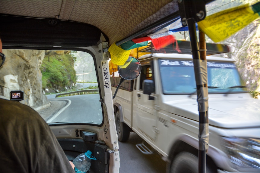 A tuk-tuk drives past a jeep on a narrow road.