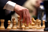 a hand touches a chess piece on a chess board