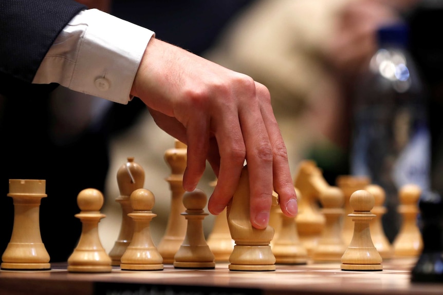 a hand touches a chess piece on a chess board