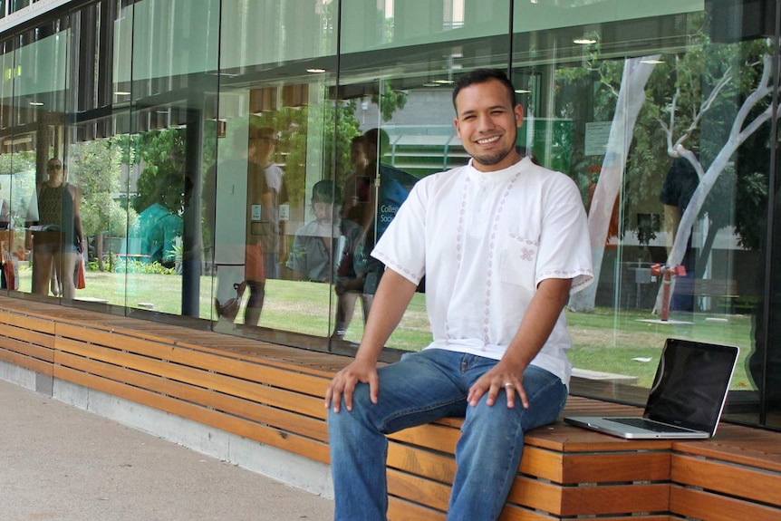 Carlos Garcea sits on a wooden bench outside the education building at James Cook University Townsville