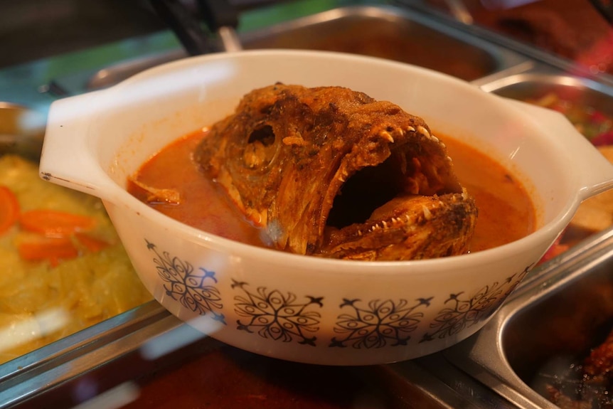 A fish head sits in a dish of curry