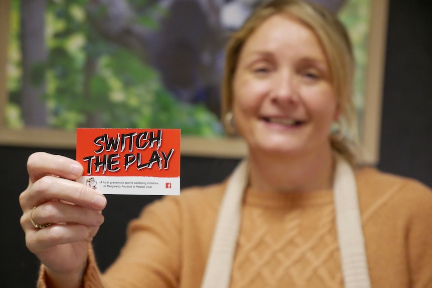 A woman holding a small card that says 'switch the play' on the front. 