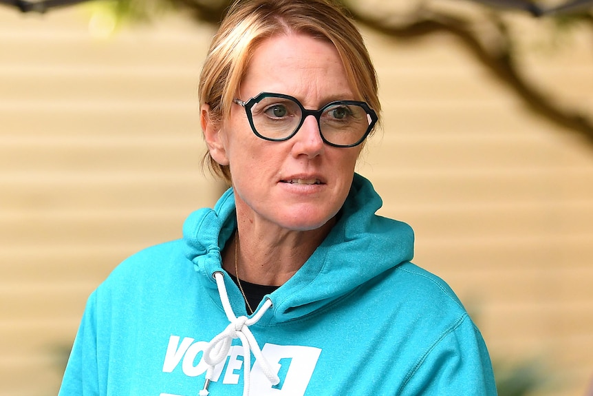 Zoe Daniel holds a coffee cup and wears a jumper with her campaign branding outside a polling booth