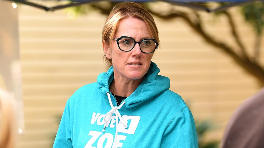 Zoe Daniel holds a coffee cup and wears a jumper with her campaign branding outside a polling booth