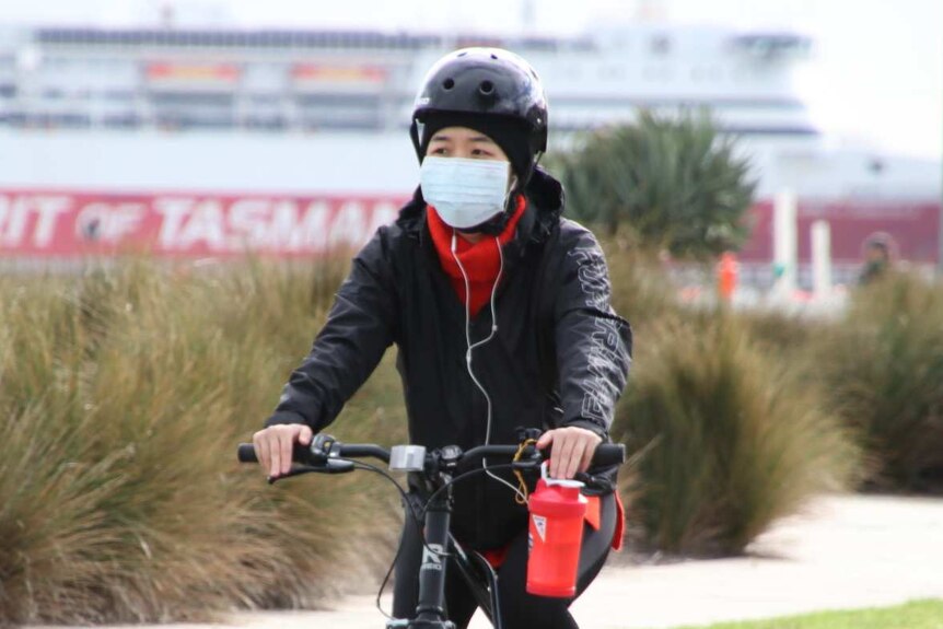 A woman wearing a surgical mask rides a bike near the Spirit of Tasmania.