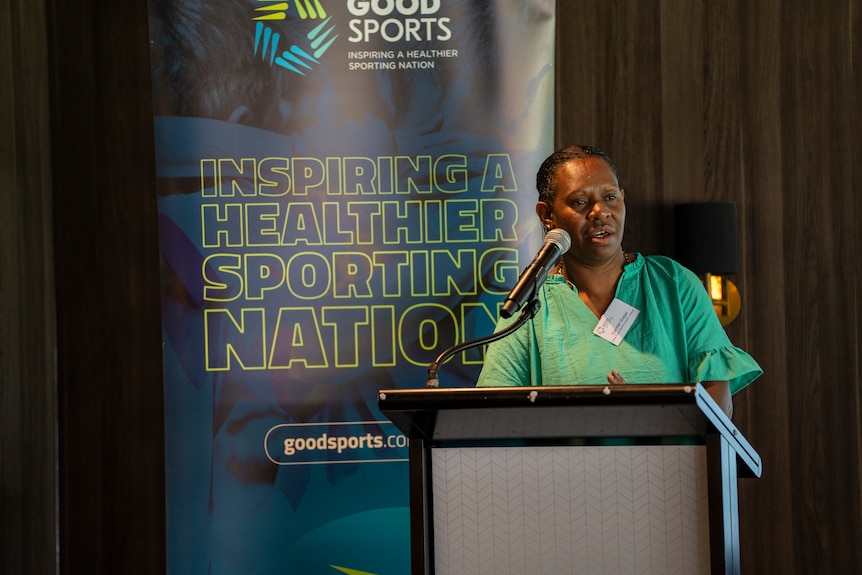 An Indigenous woman representing a rugby league club stands at a podium making a speech during a community sports launch.