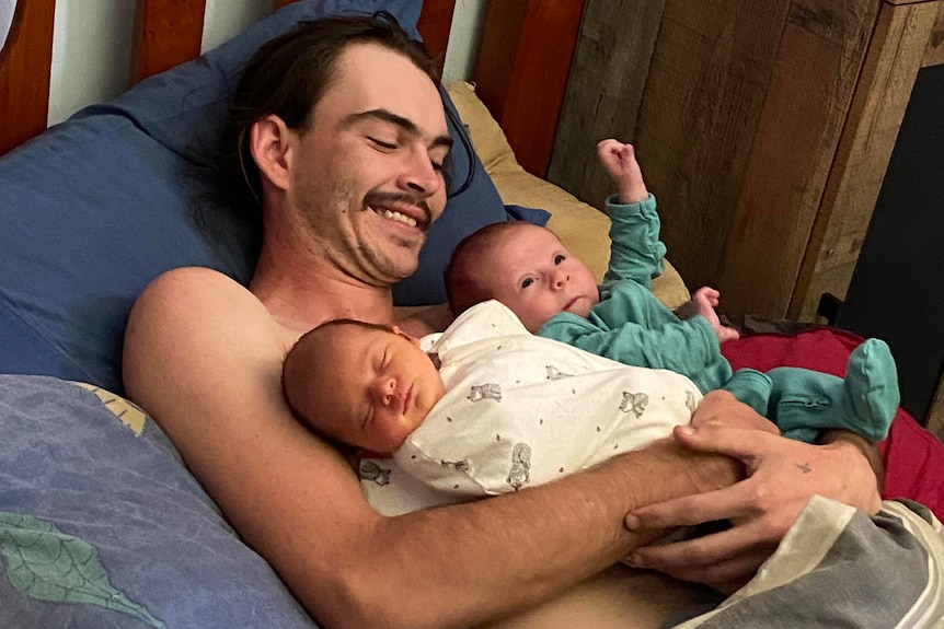 Man plays in bed holding two babies.