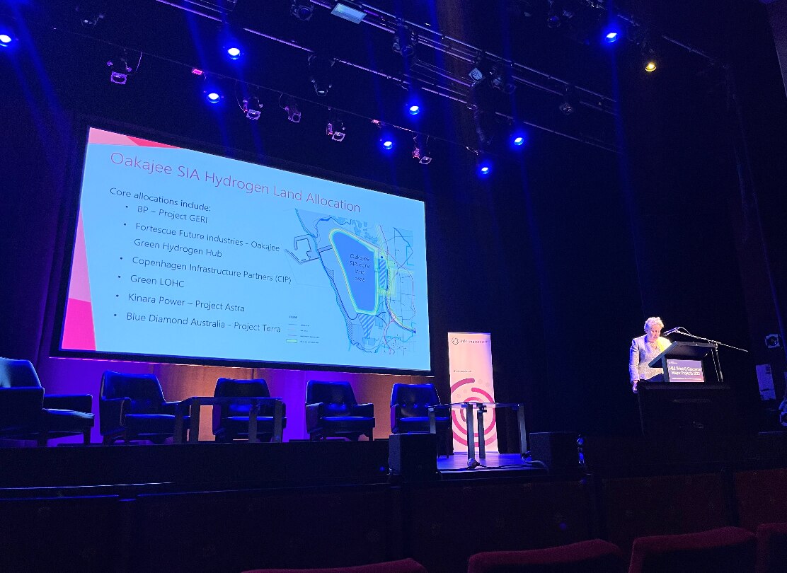 Slide showing a map image with woman at lectern in front of dark stage 