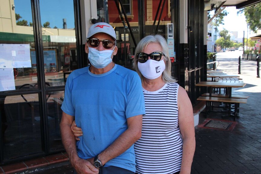 A man and a woman wearing masks pictured in an outdoor alfresco area