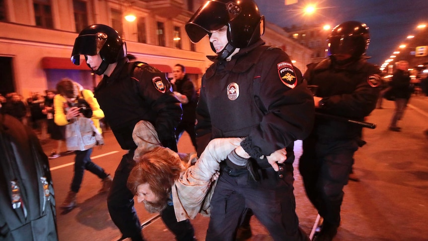 Three riot police officers detain a protester during a rally in St Petersburg. They are carrying him by his arms and legs.