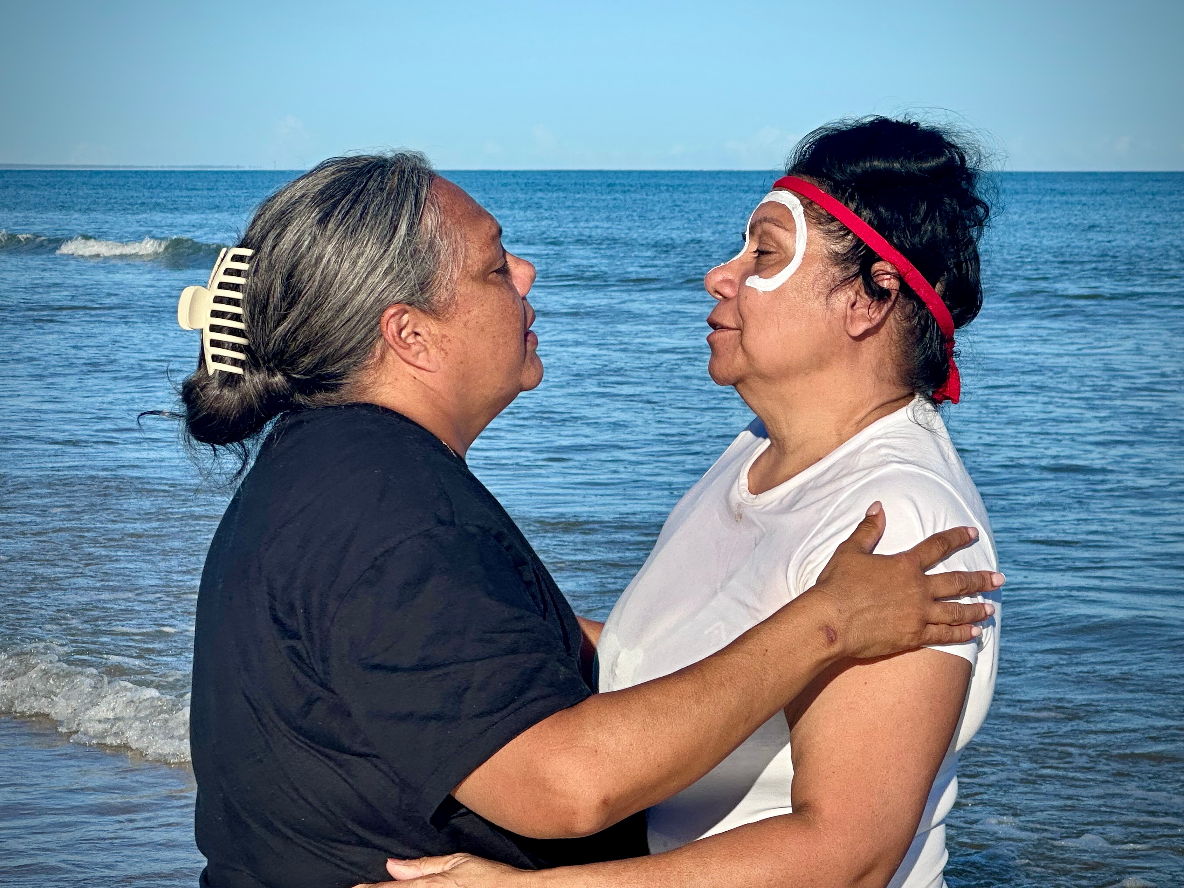 Two people standing in the water, holding one another with their eyes closed.