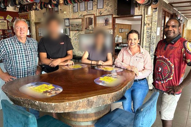 Five people smile at the camera in what looks like a pub. Three faces are clear, two blurred.