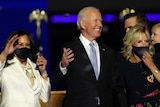 Joe Biden smiles, standing in front of Kamala Harris and Jill Biden as they celebrate his presidential election win