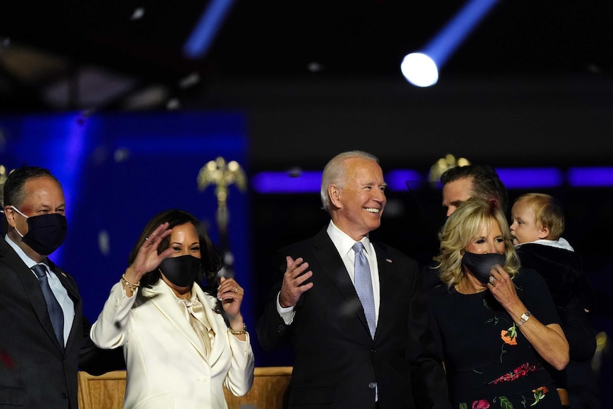Joe Biden smiles, standing in front of Kamala Harris and Jill Biden as they celebrate his presidential election win