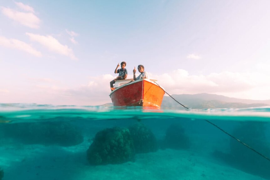 This image shows two children in the boat, the stunning view beneath the waves, as well as the beautiful sky.