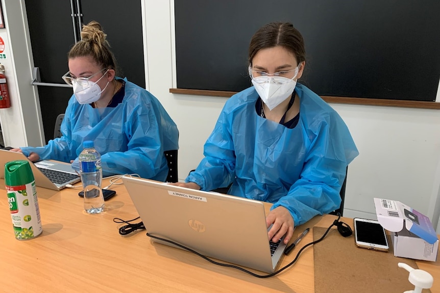 two women in ppe on their laptops sitting down at a table