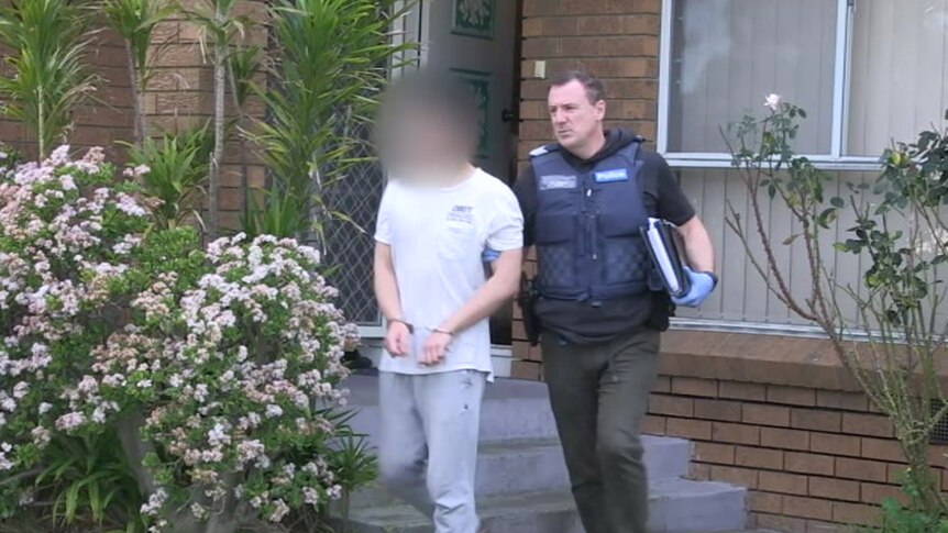 A handcuffed youth is led away from a home in Melbourne's south-east by a police officer.